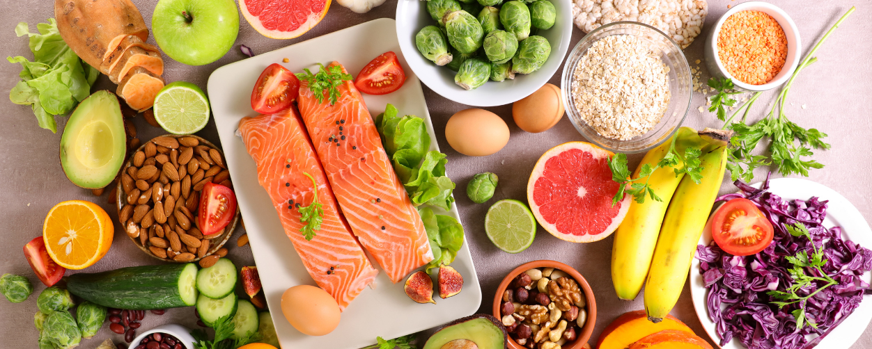 This is a picture of a variety of nutritious foods that are bright and laid out on a table including salmon, almonds, bananas, cucumber and other items.